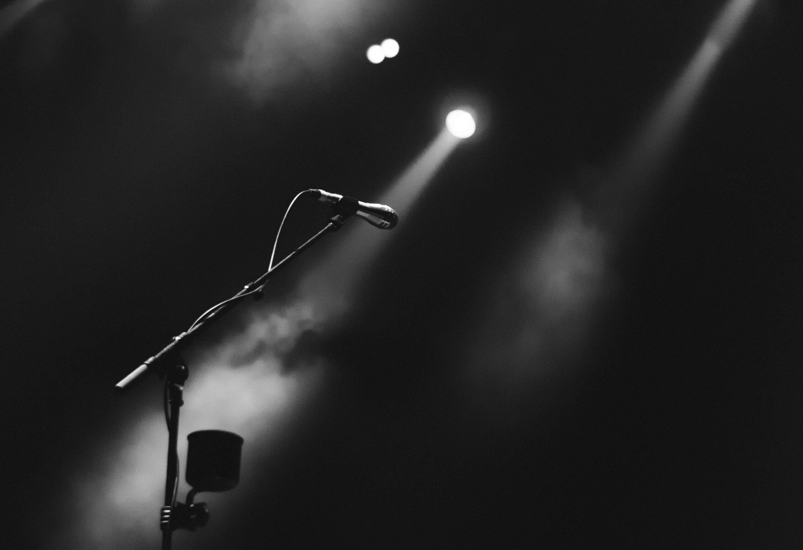 A black and white photo depicting a spotlight shining on a stage microphone. Cover image used for an article about new SongVest SongShare offerings and a new VIP auction.