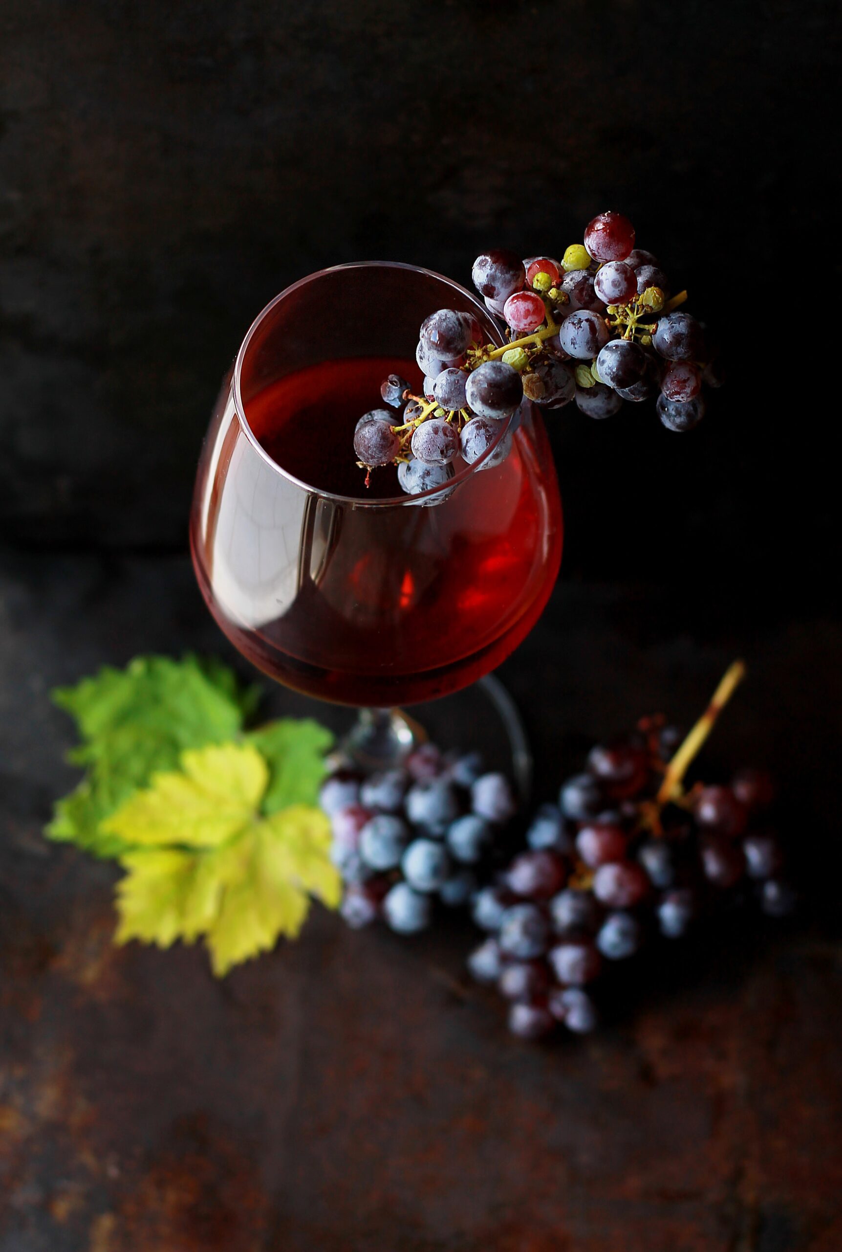 Depicts a glass of wine near grapes and grape leaves. Used as a photo to represent wine as an alternative asset class.