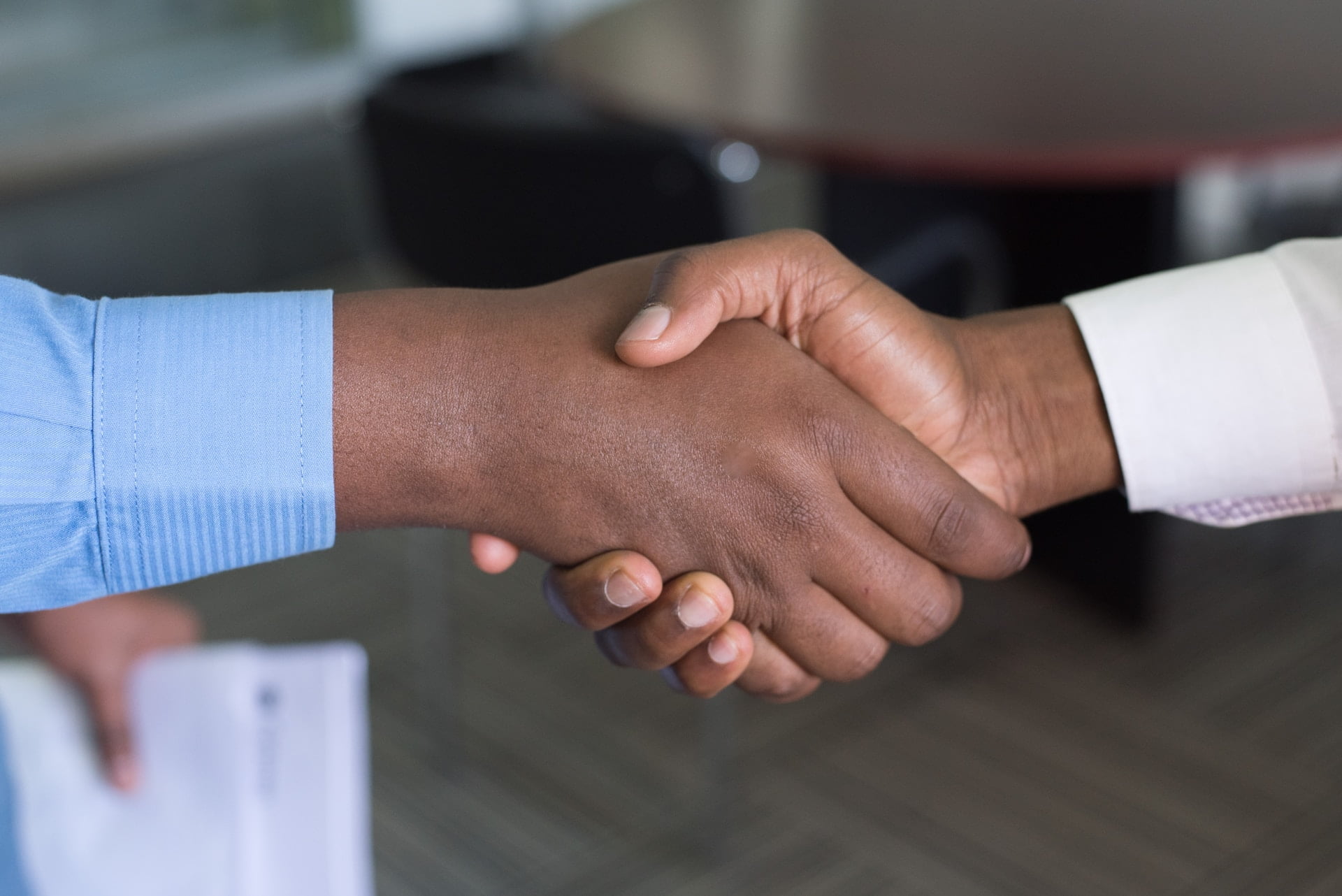 Depicts two people shaking hands in an office setting. Used as a cover image for a news article about StartEngine completing their acquisition of SeedInvest.