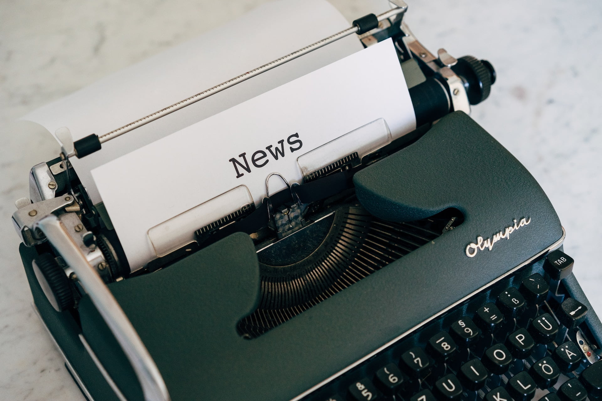 Depicts a typewriter with a piece of paper that says "News" on it. Used as a cover image for an article covering alternative investment news.