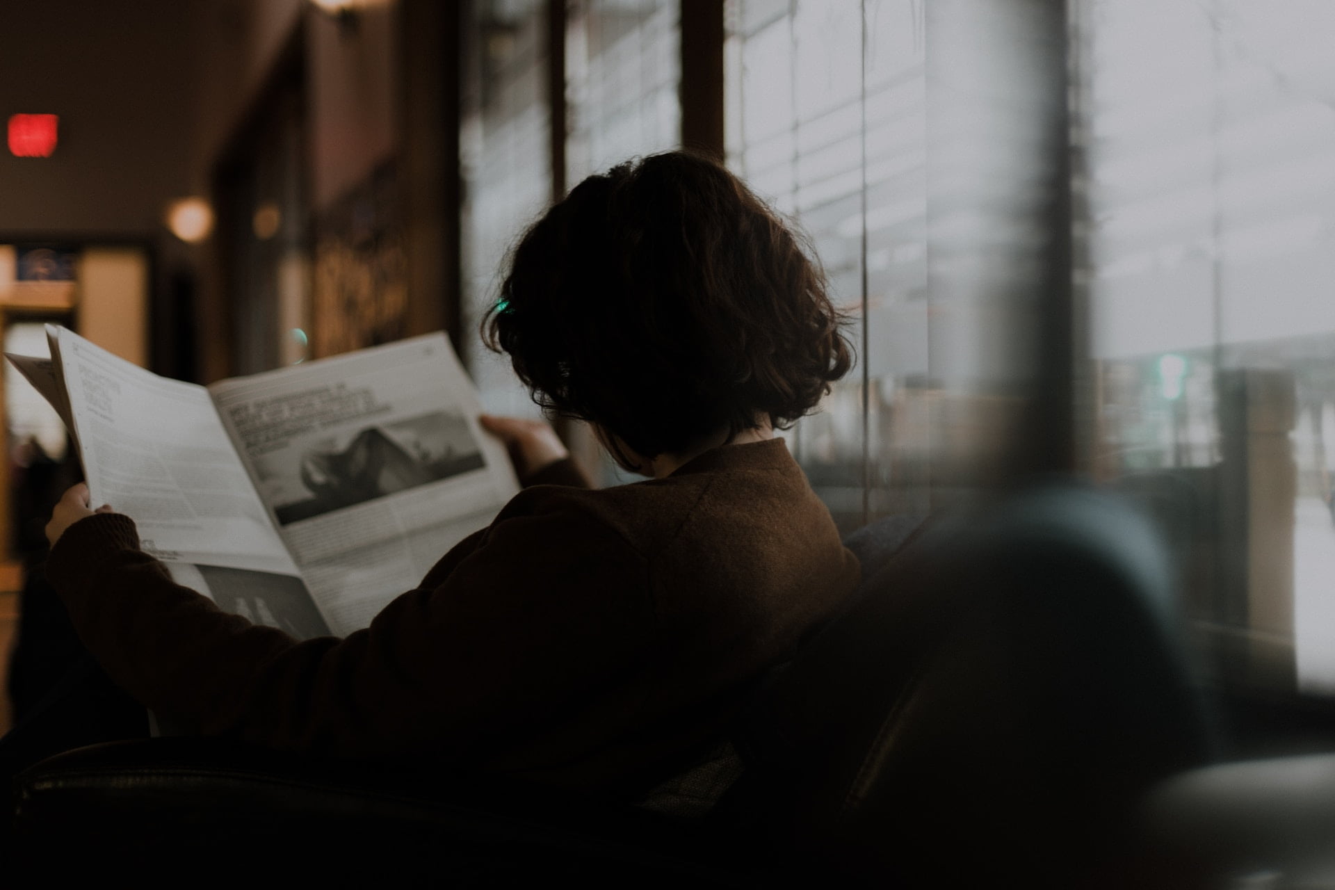 Depicts a woman reading a newspaper. Used as a cover image for an article rounding up news stories about alternative asset investing.